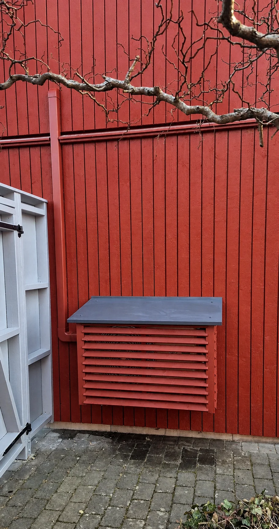 Rödmålat träskydd för värmepump på röd träfasad